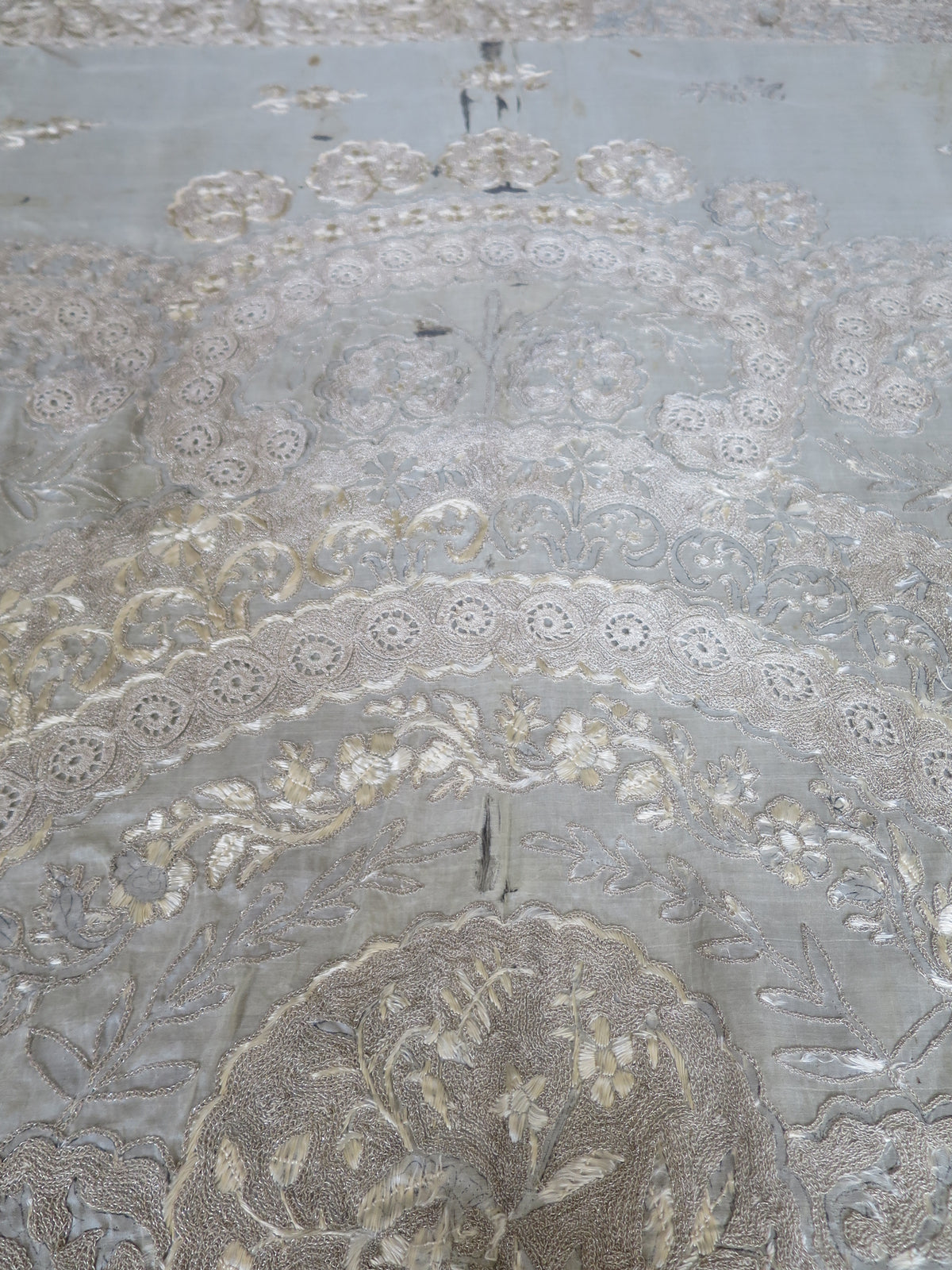 Close up of vertical splitting and shattering on the delicate silk gauze background of a heavy antique Zardozi textile.