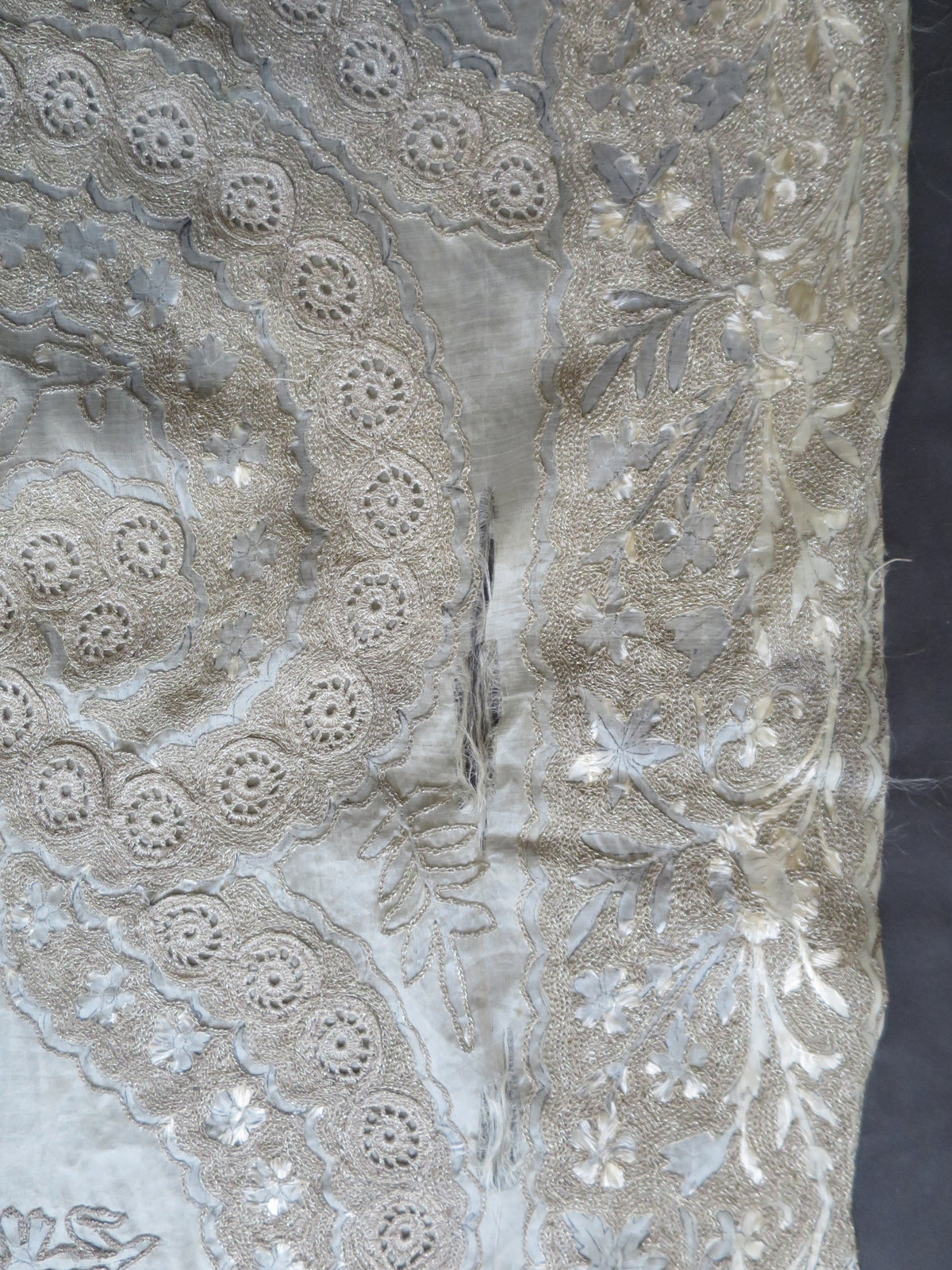 Close up of vertical splitting and shattering on the delicate silk gauze background of a heavy antique Zardozi textile.