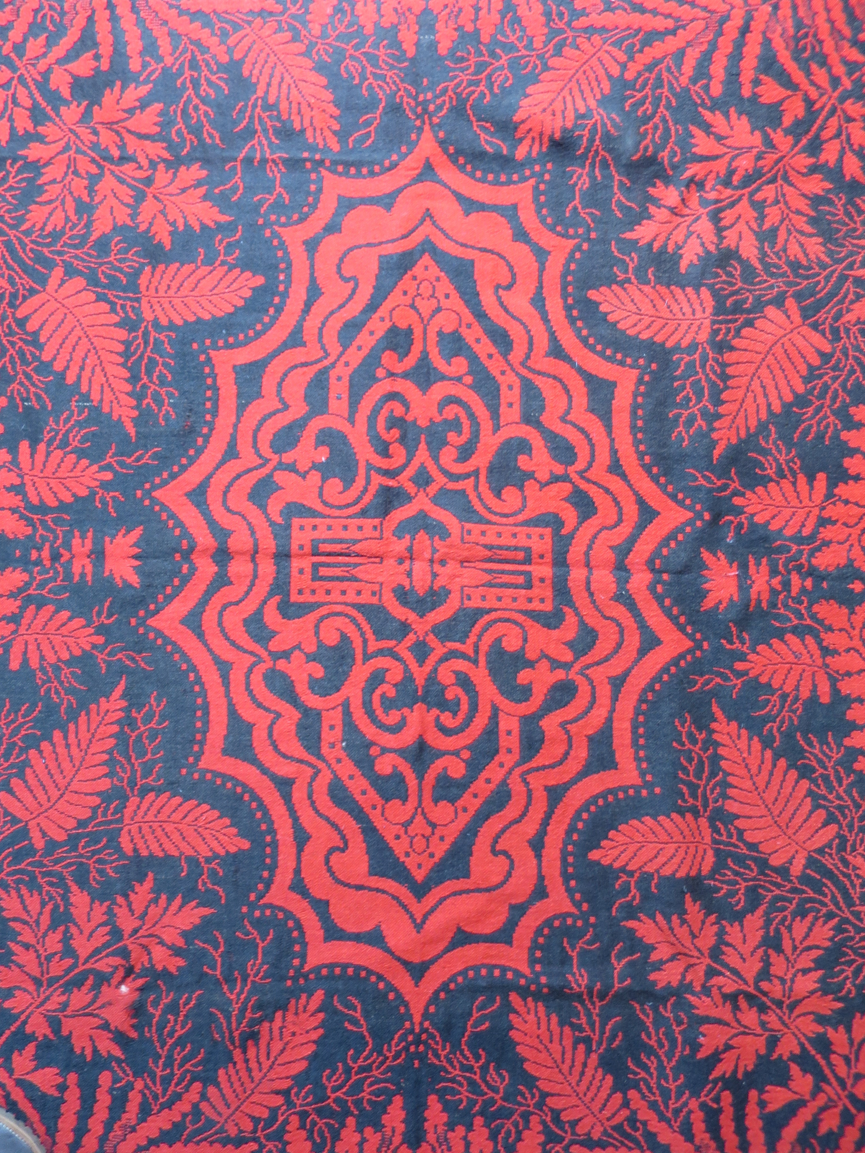 Central medallion of a 19th-century American Jacquard coverlet, featuring a reversible madder-red and indigo-black geometric and scrollwork design.