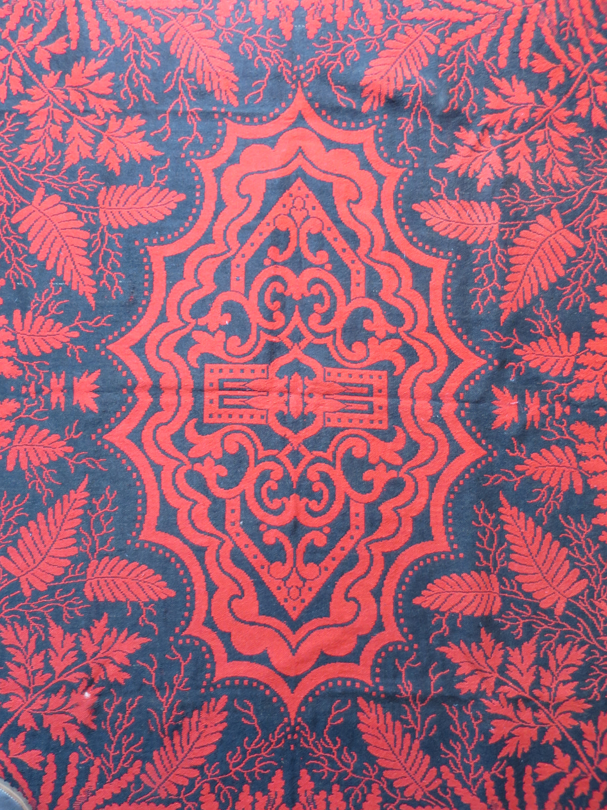 Central medallion of a 19th-century American Jacquard coverlet, featuring a reversible madder-red and indigo-black geometric and scrollwork design.