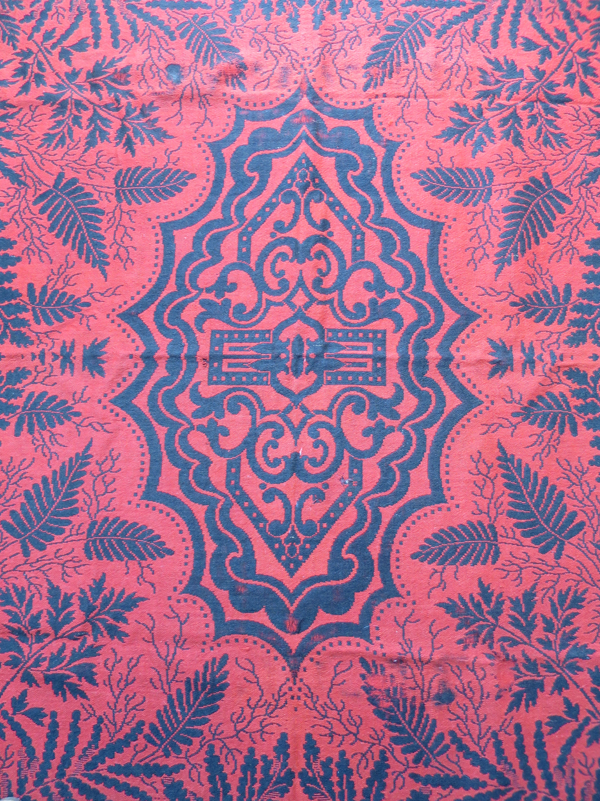 Reversible side of an antique Jacquard coverlet, showing the inverted colorway with a predominantly madder-red background and dark indigo pattern.
