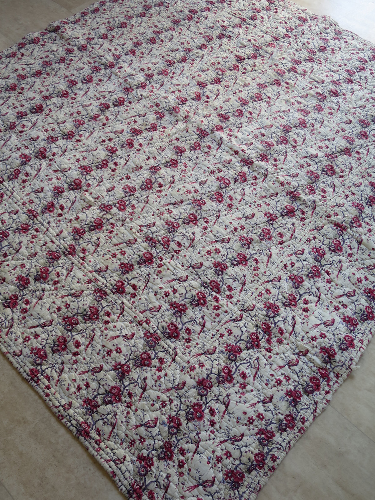 French piqué quilt with a block-printed front showing long-tailed birds among floral trails.