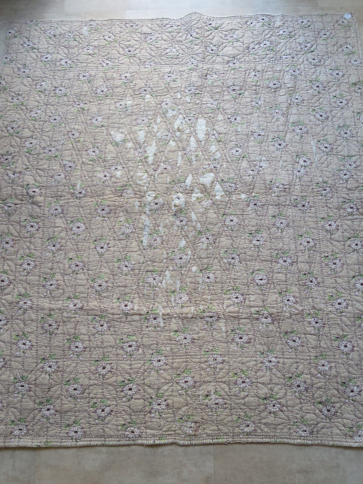 Worn centre of the quilt’s floral reverse, where printed cotton has been lost and white wadding is exposed.