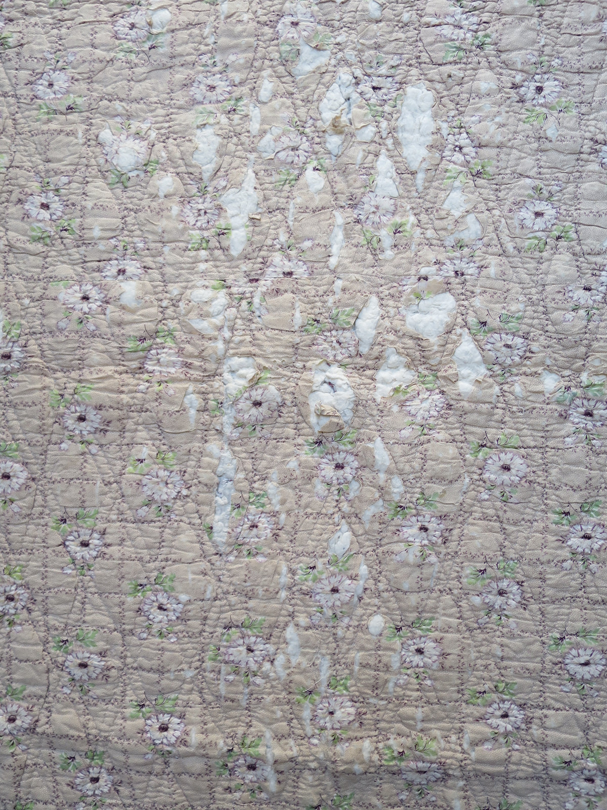 Closer view of fabric loss and exposed white wadding at the centre of the quilt’s reverse.