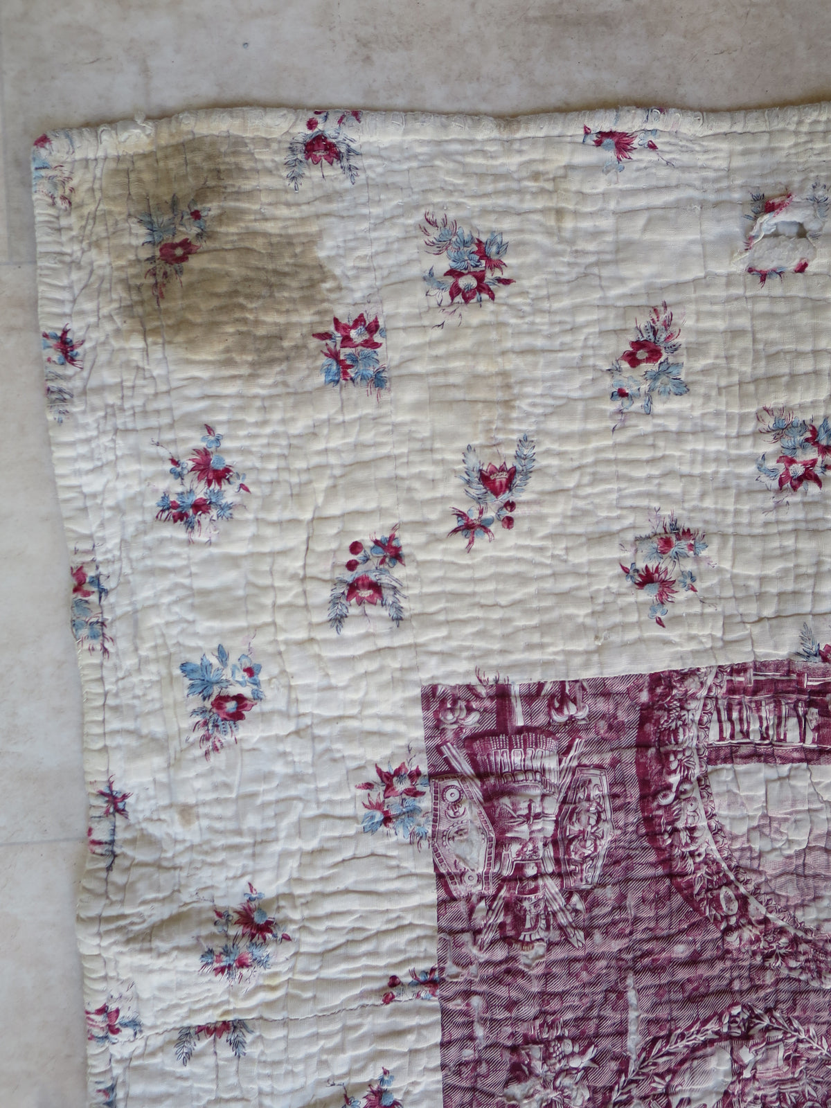 Staining near a corner of the quilt’s cream border with red and blue floral sprigs