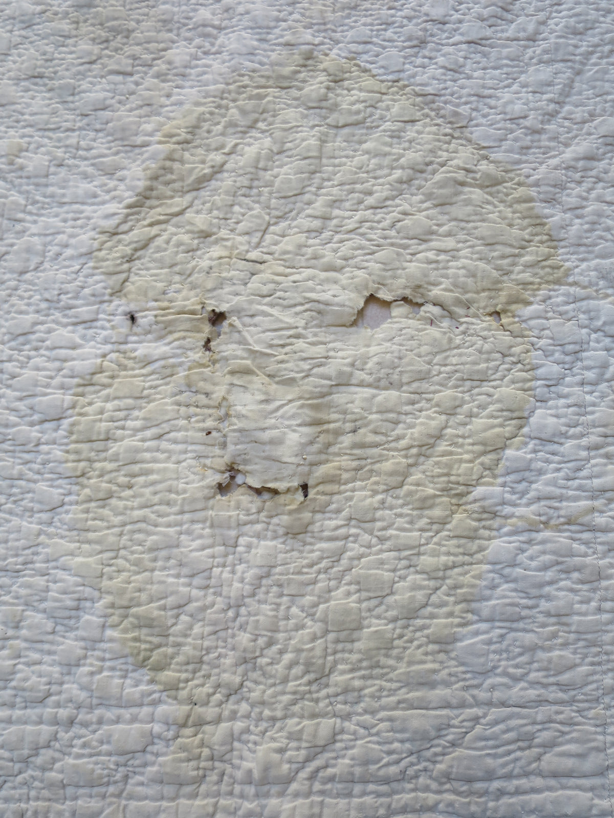 Unmended damage on the quilt’s reverse, where staining and holes through the fabric are visible.