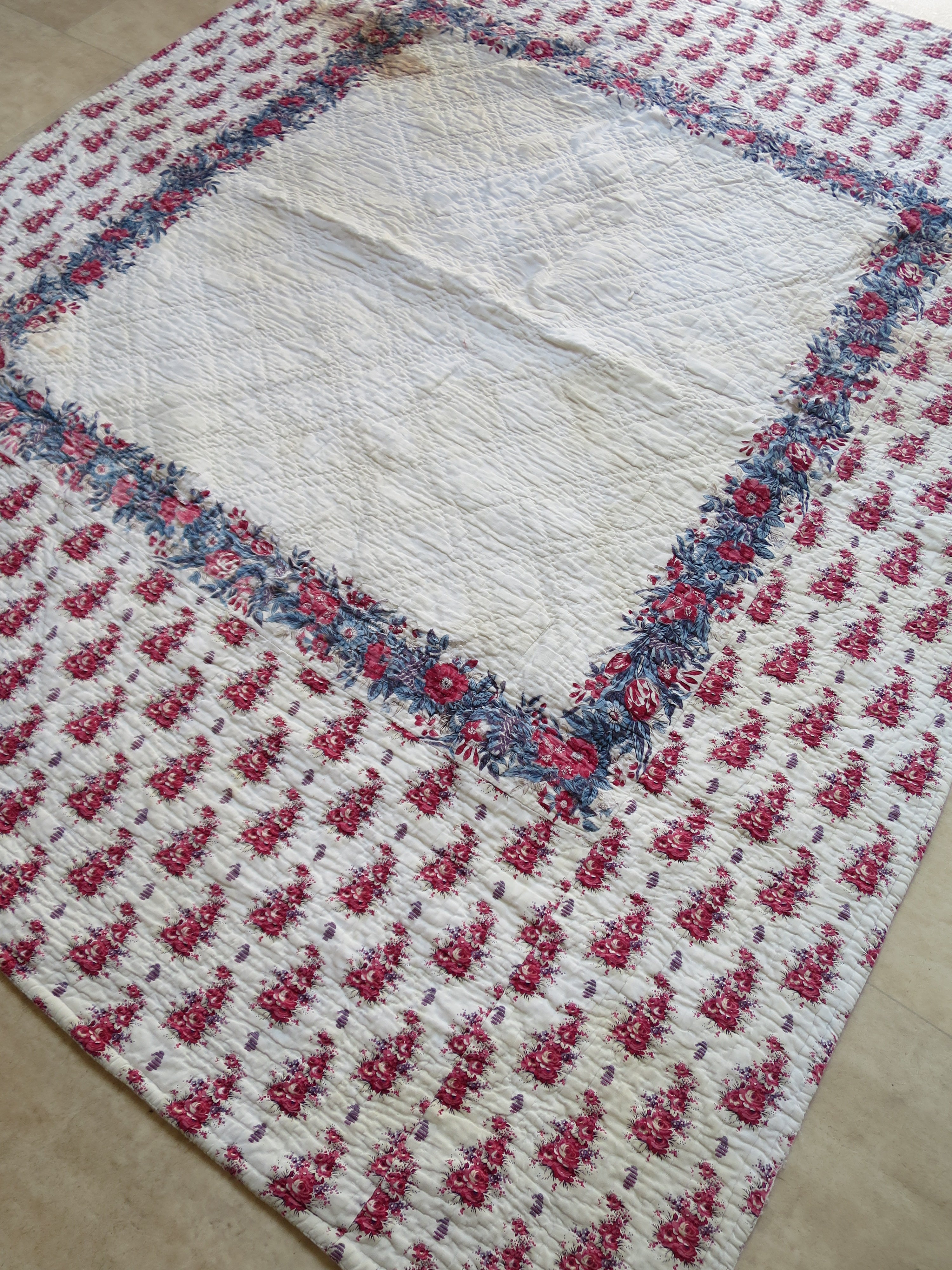Early 19th-century French quilt, printed front with a central floral scarf and wide quilted border.