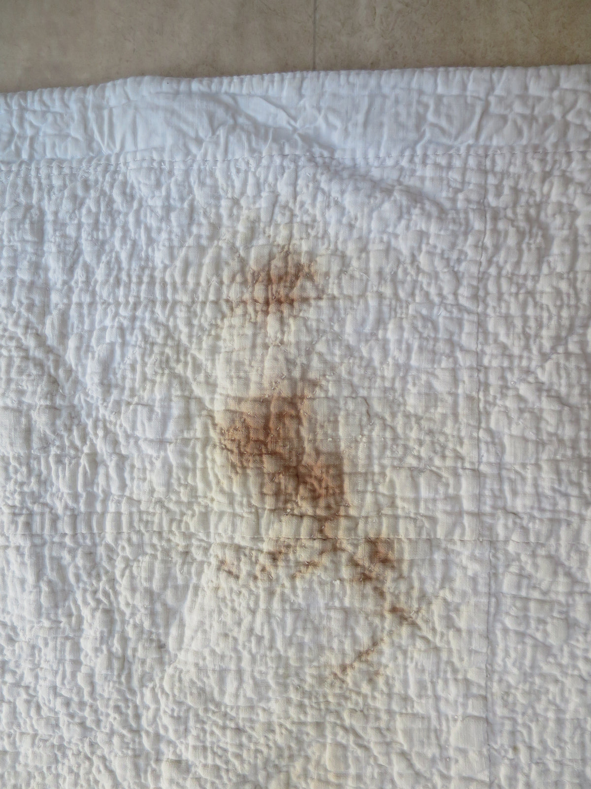 Dark rust-coloured staining on the white quilted reverse of the French quilt.
