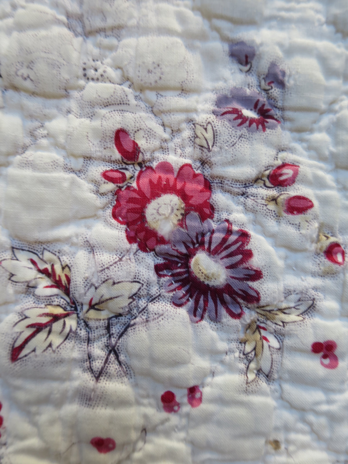 Block-printed floral sprigs in pink, and purple surrounded by picotage on the front of the French quilt.