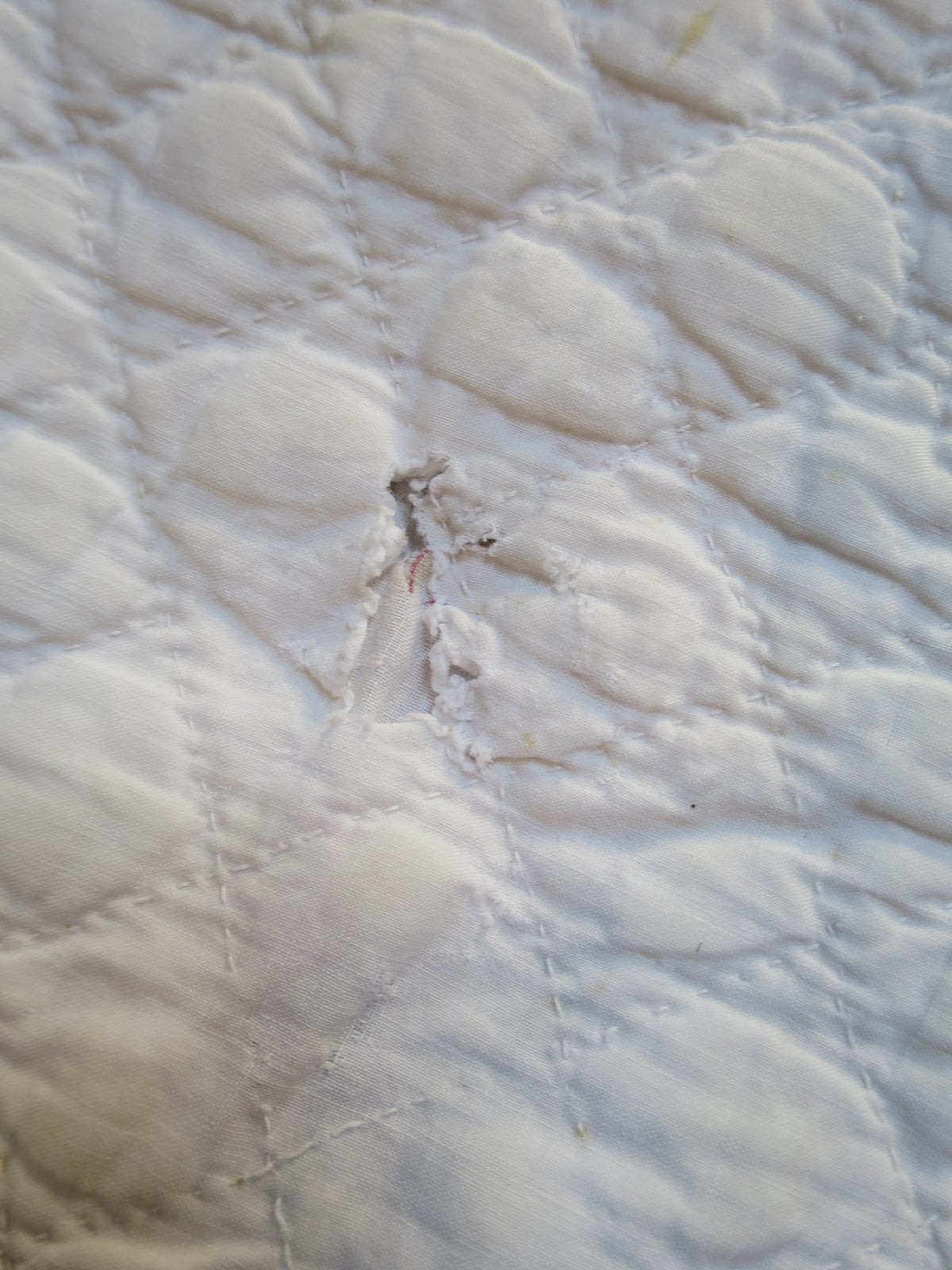 Area of wear on the white reverse, with the surrounding corded quilting visible.